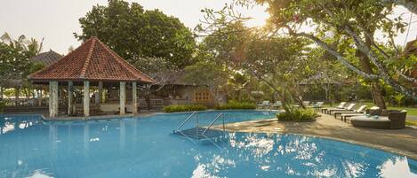 A swimming pool with a gazebo, lounge chairs, and lush greenery.