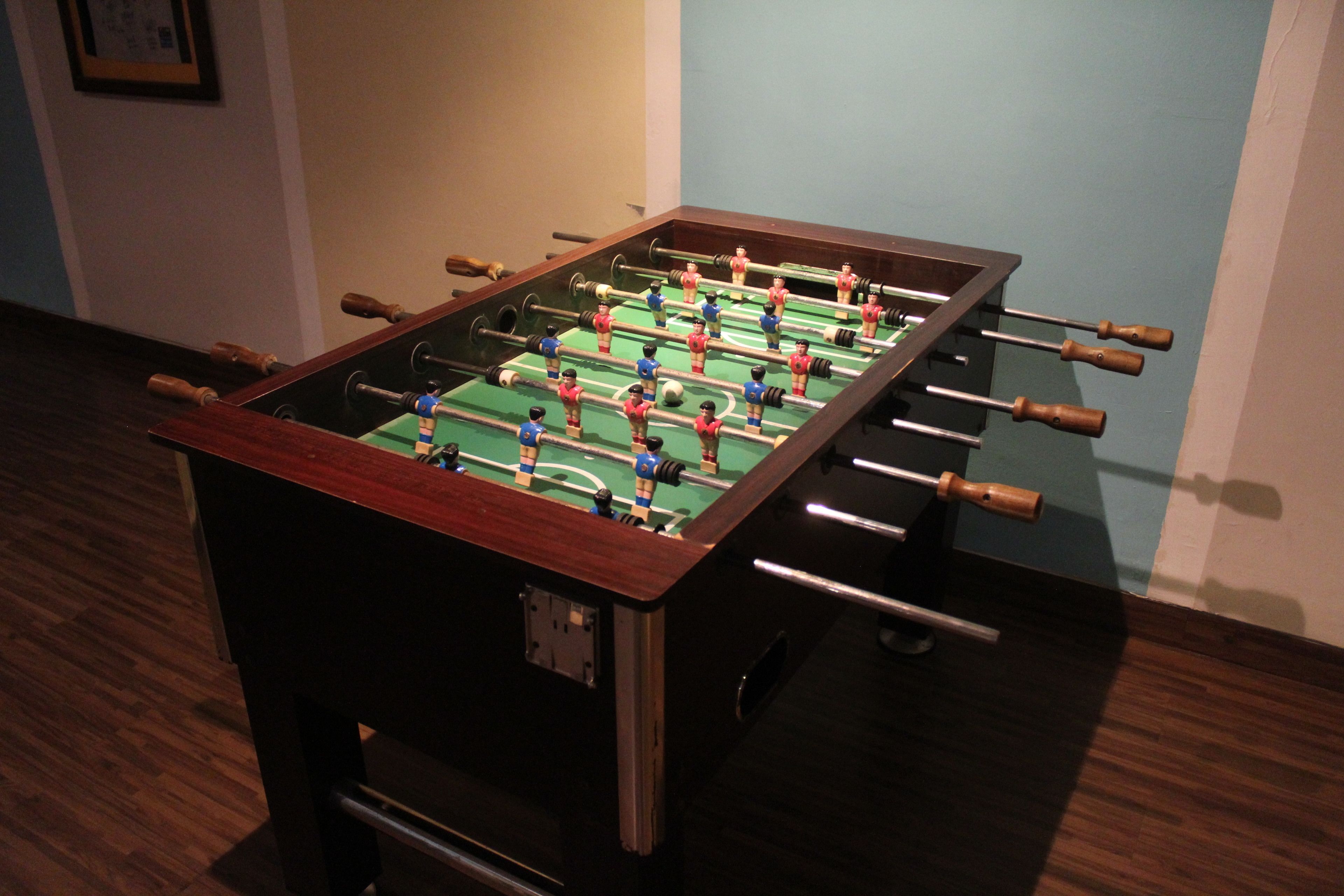 A foosball table with a wooden frame and metal rods, set on a dark wooden floor.