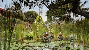 Un jardín sereno con un estanque, rodeado de abundante vegetación y árboles.