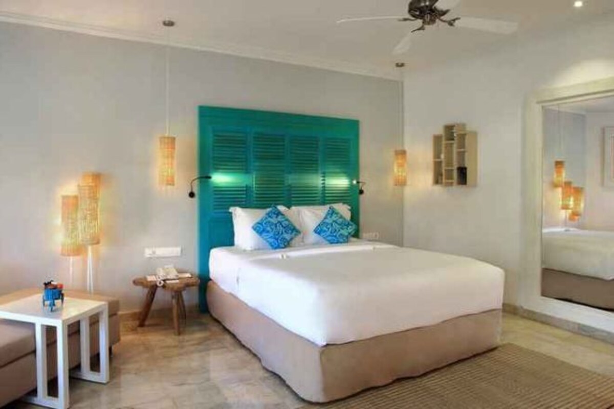 A hotel room with a bed, bedside tables, a ceiling fan, and a large window.