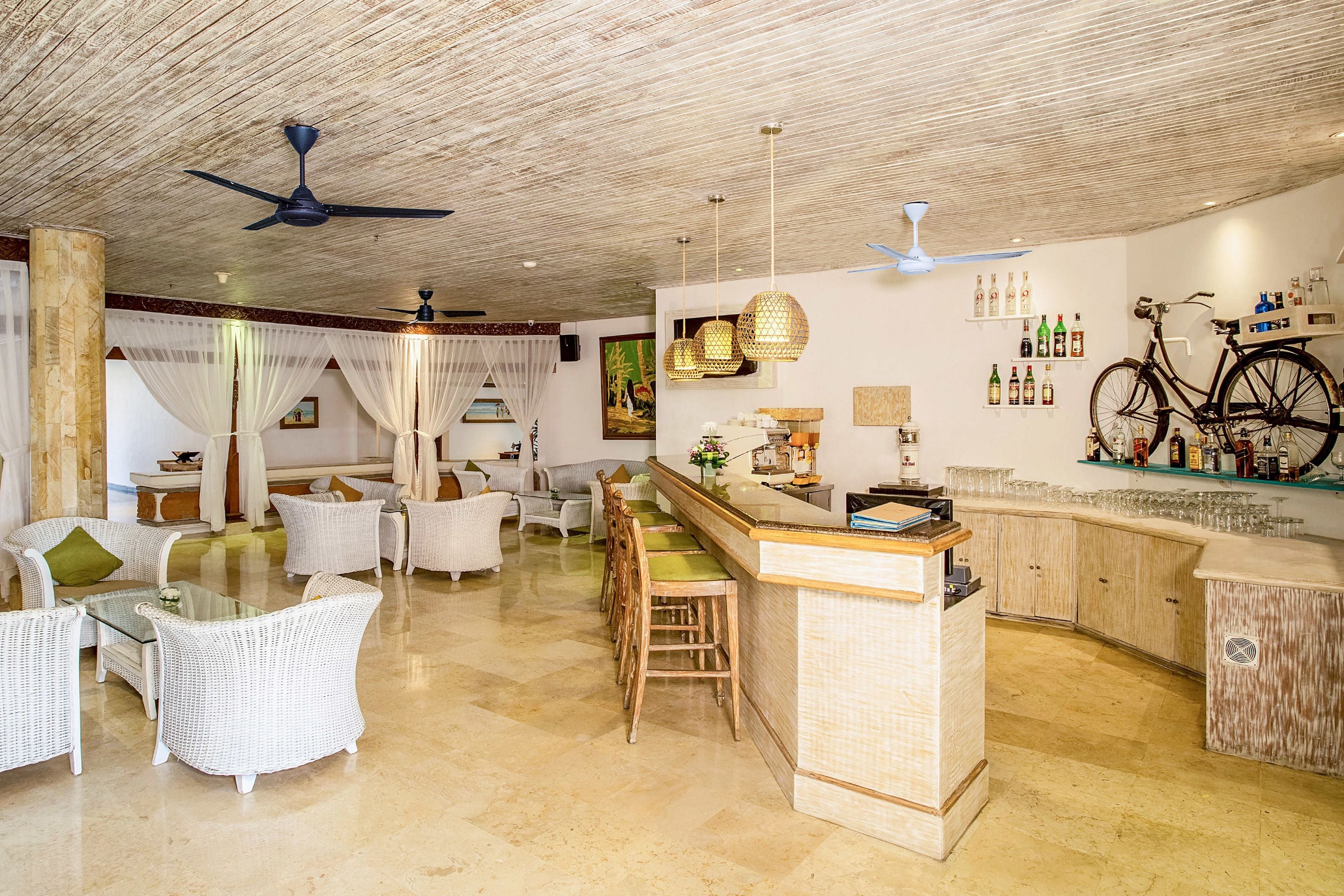 A spacious living area with a bar, white wicker furniture, and a ceiling fan.