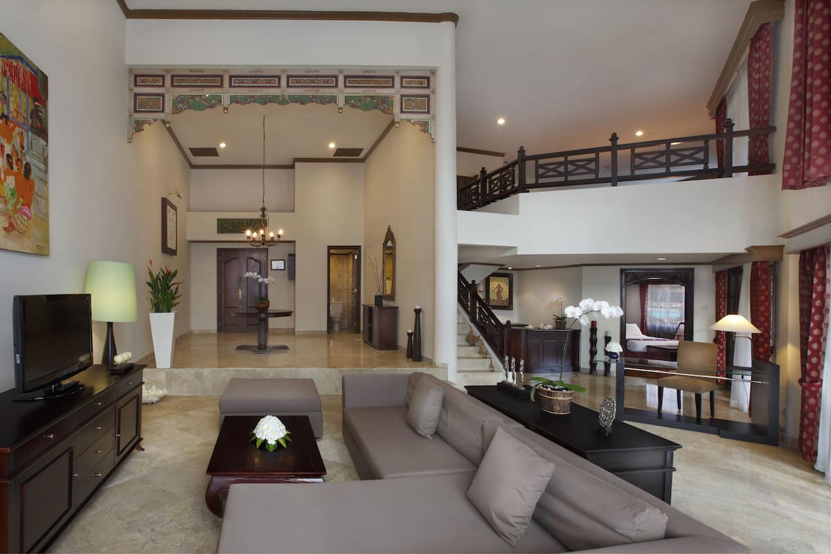 A spacious living area with a sofa, a coffee table, and a TV on a cabinet. There is a staircase leading to an upper level with a balcony.