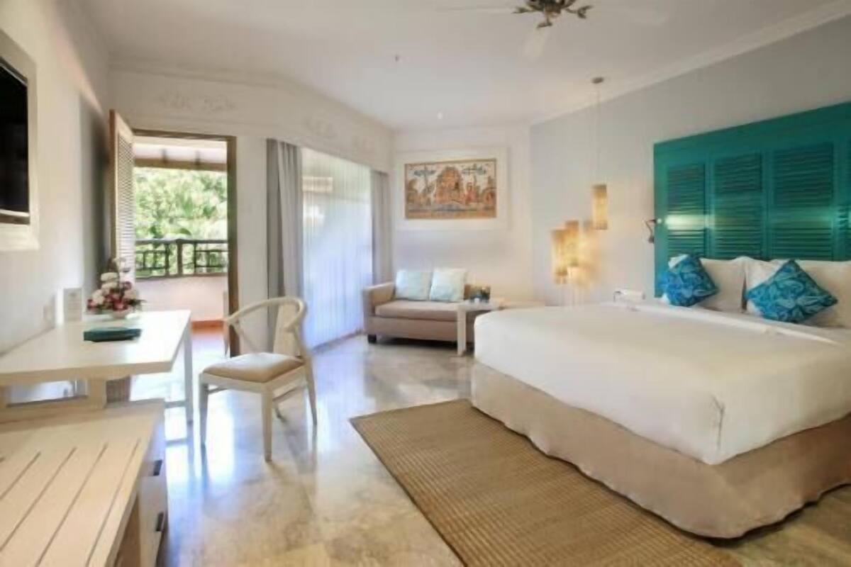 A hotel room with a bed, a desk, a chair, a sofa, and a balcony with a view.