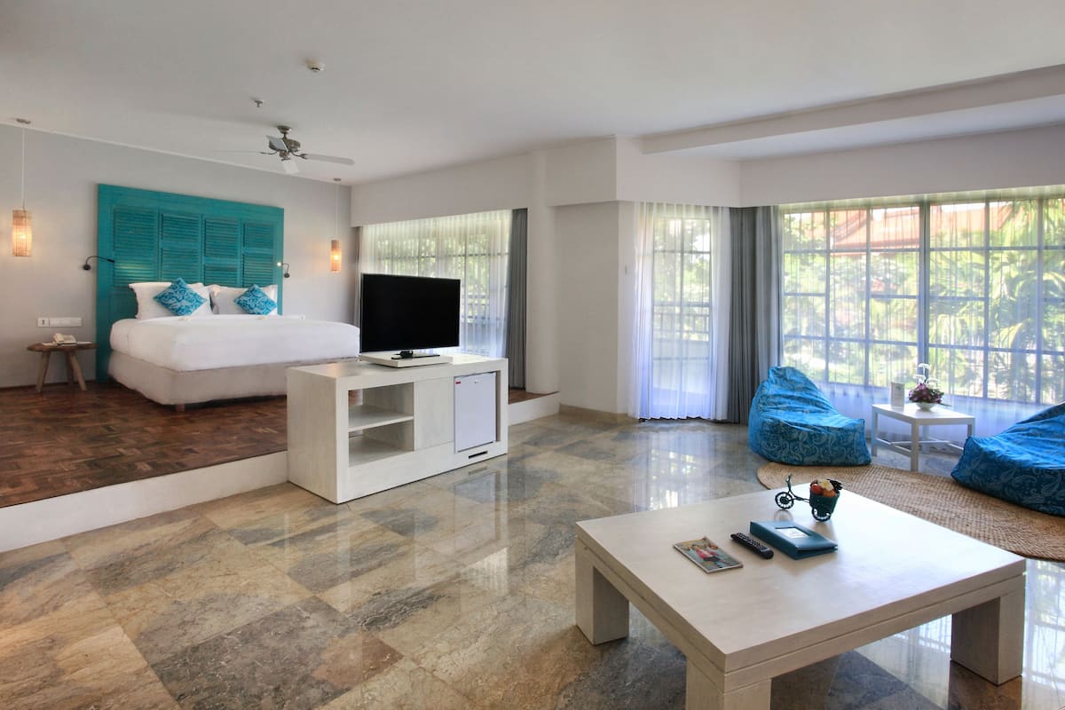 A modern hotel room with a bed, a TV, a coffee table, and a seating area with bean bags.