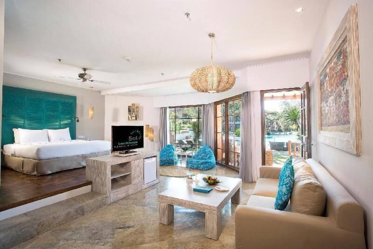 A modern hotel room with a bed, sofa, coffee table, TV, and a view of the outdoors.