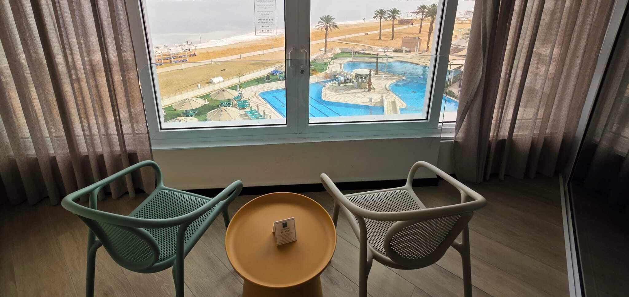 Una habitación con dos sillas y una mesita, una ventana con vistas a una piscina y la playa.
