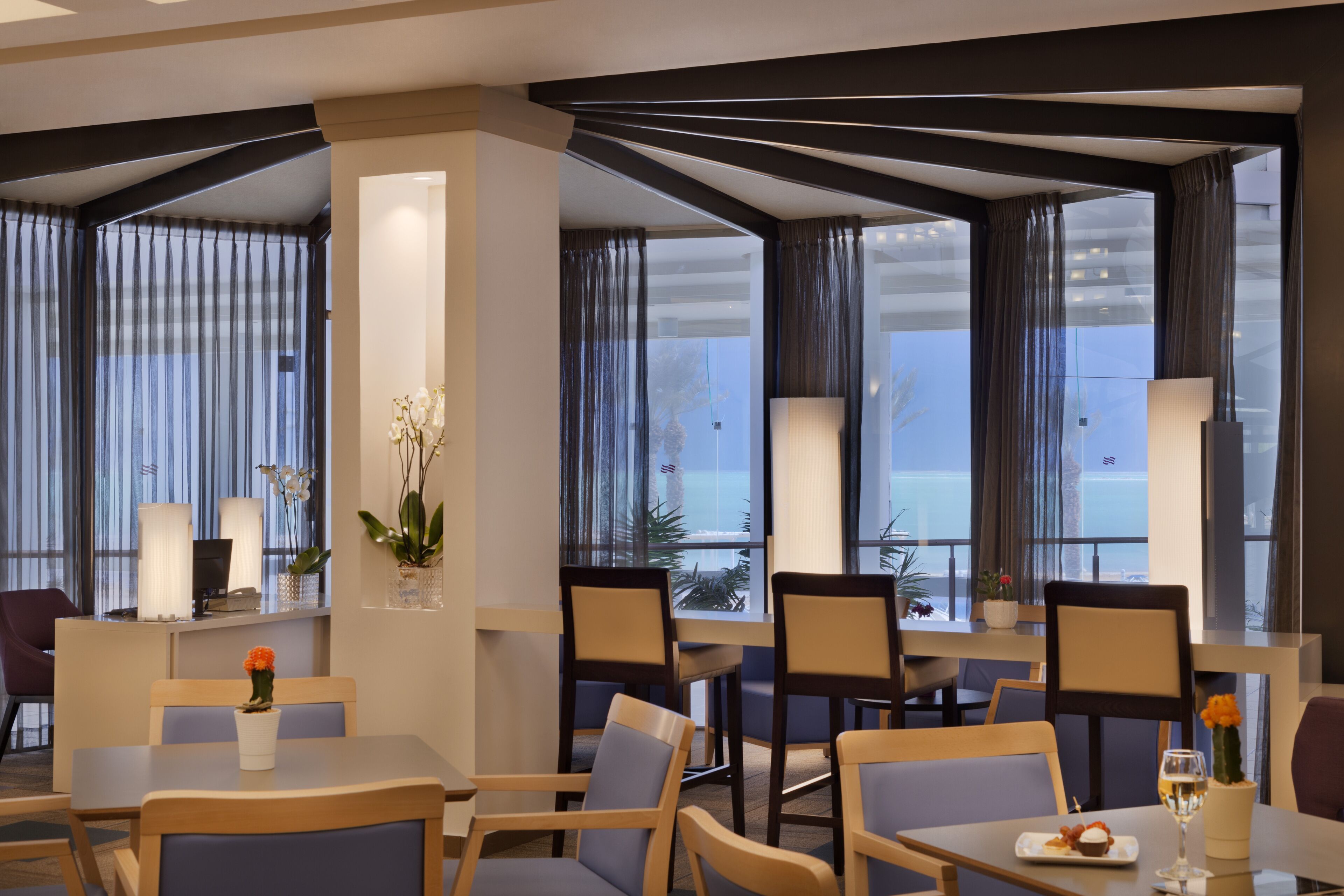 A modern hotel lobby with seating areas, large windows, and decorative plants.