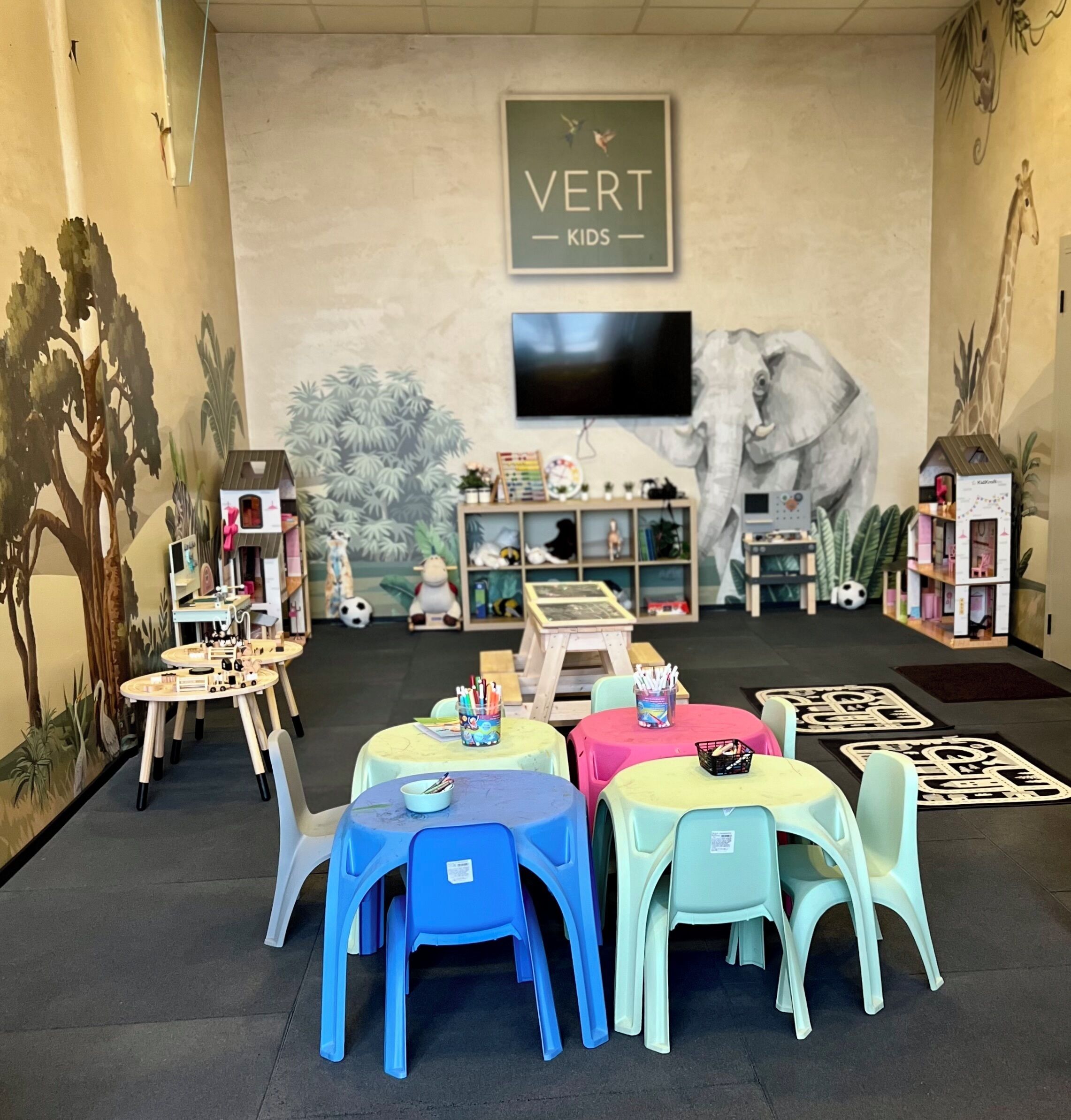 A children's play area with colorful tables and chairs, educational toys, and a mural of an elephant.