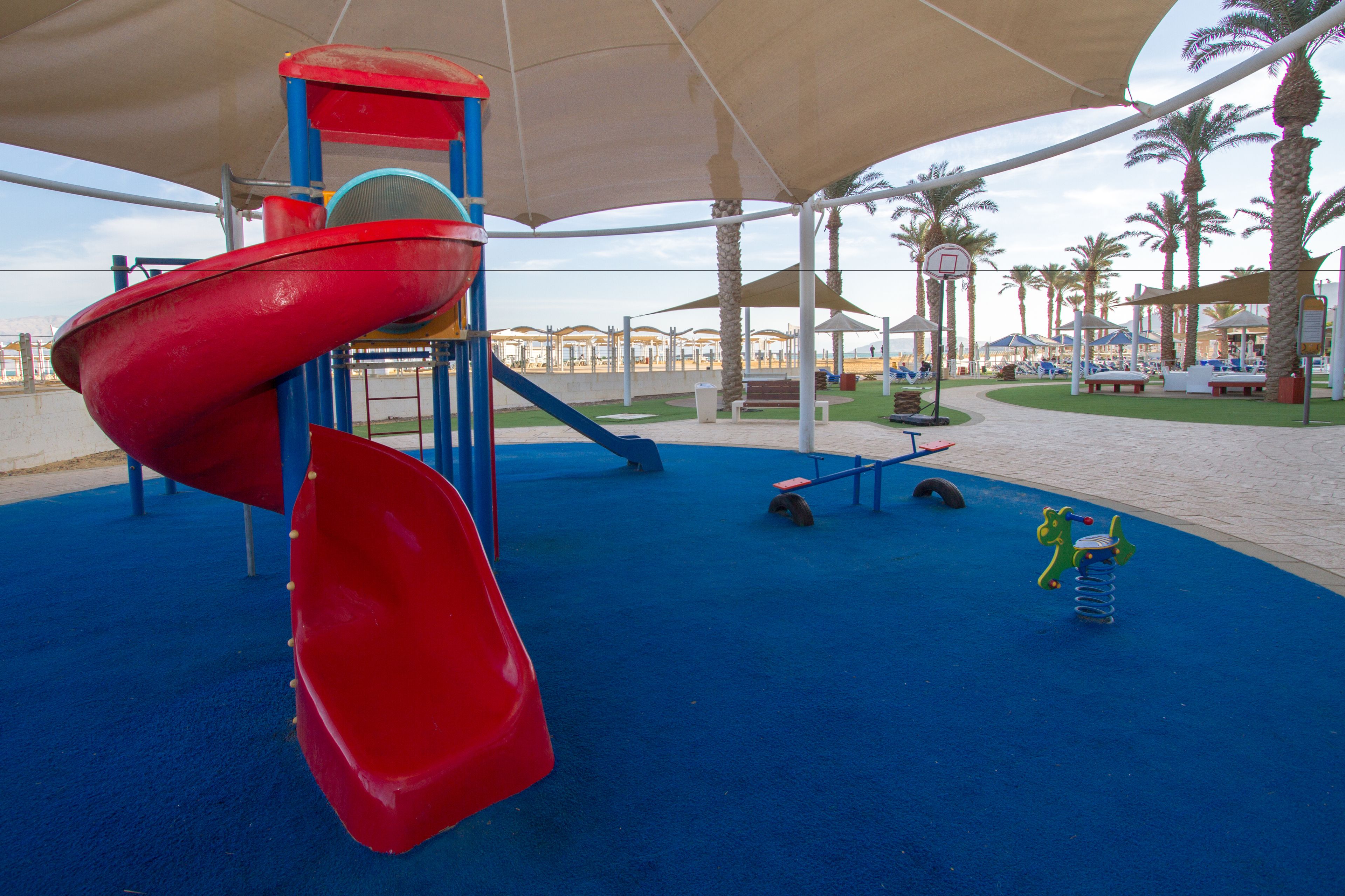 A playground with a red slide, blue and red play structures, and a blue rubberized floor.