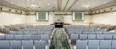 Un salón de conferencias con filas de sillas, un escenario y dos pancartas con la leyenda 'VERT' y 'DEAD SEA'.