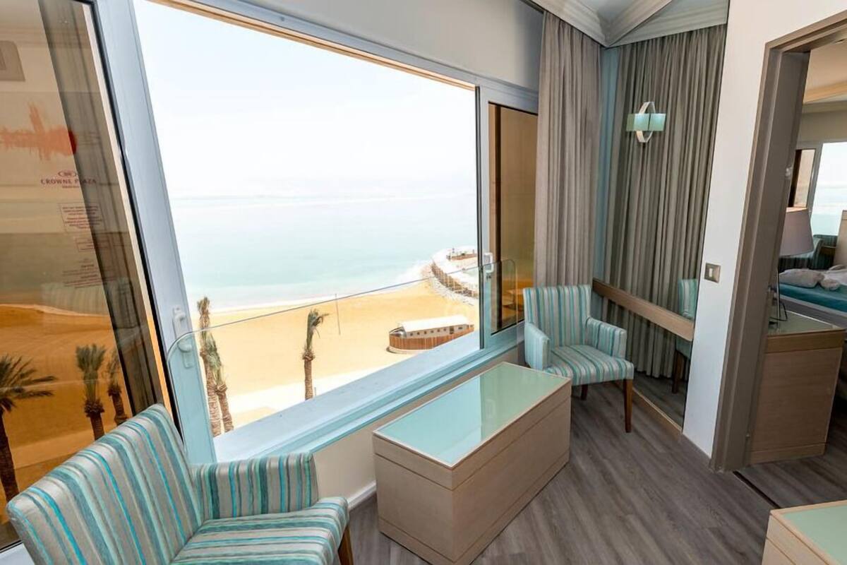 A hotel room with a large window, a bed, a seating area with chairs, and a small table.