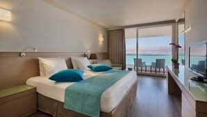 Habitación de hotel con una cama grande, un escritorio con televisor y vista al mar.