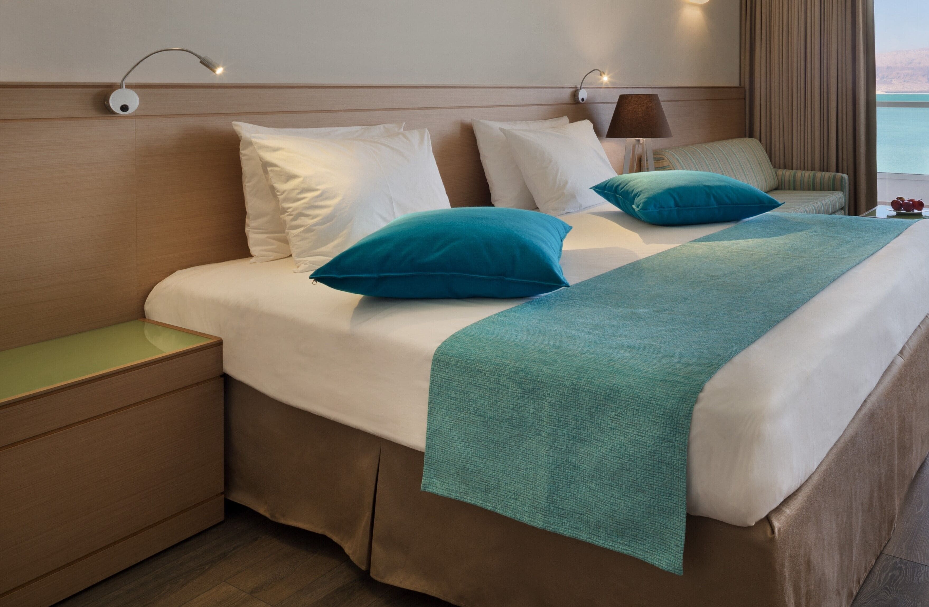 A hotel room with a bed, nightstands, a lamp, and a view of the sea.