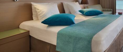 A hotel room with a bed, nightstands, a lamp, and a view of the sea.