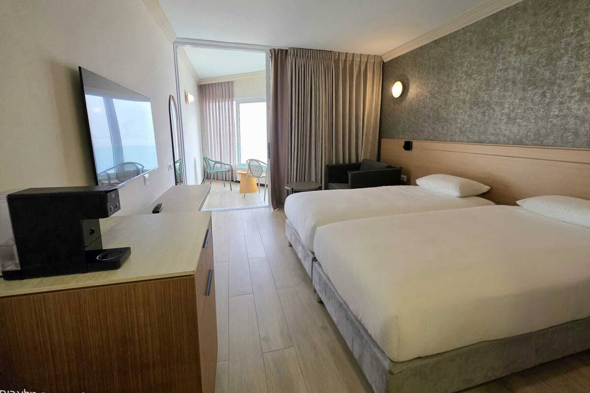 A hotel room with a bed, a desk with a computer, a TV, and a view of the outdoors.