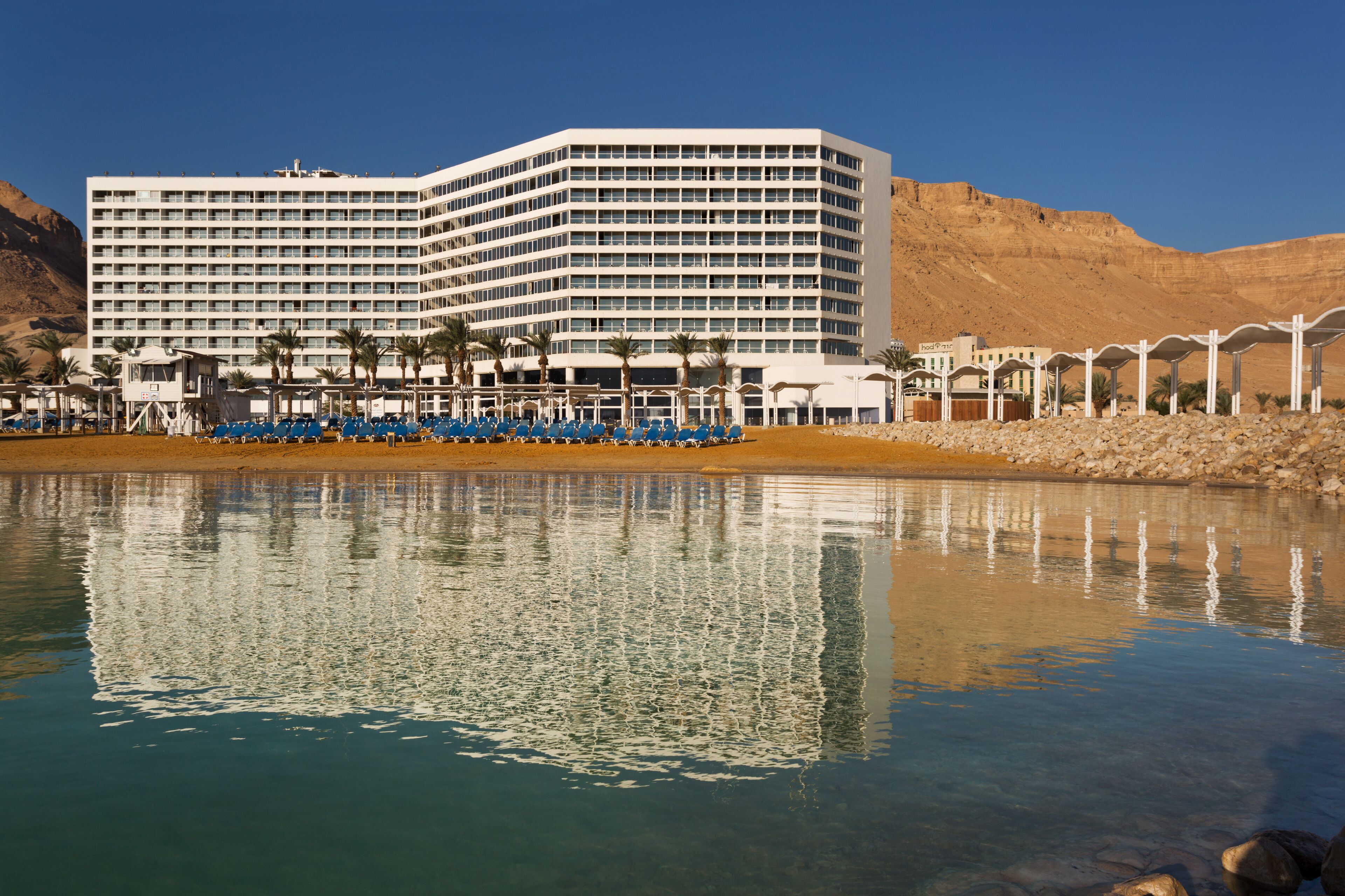 A large hotel with multiple floors, a pool in the foreground, and a desert landscape in the background.