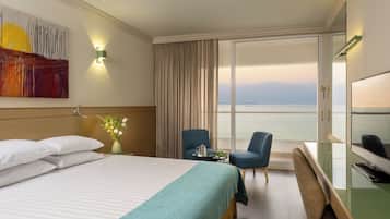 Hotelkamer met een bed, bureau, twee stoelen, televisie en een groot raam met uitzicht op zee.