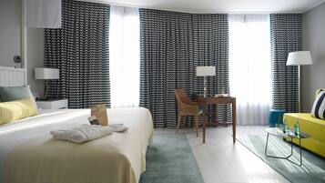 A hotel room with a bed, a desk, a chair, a lamp, and a sofa.