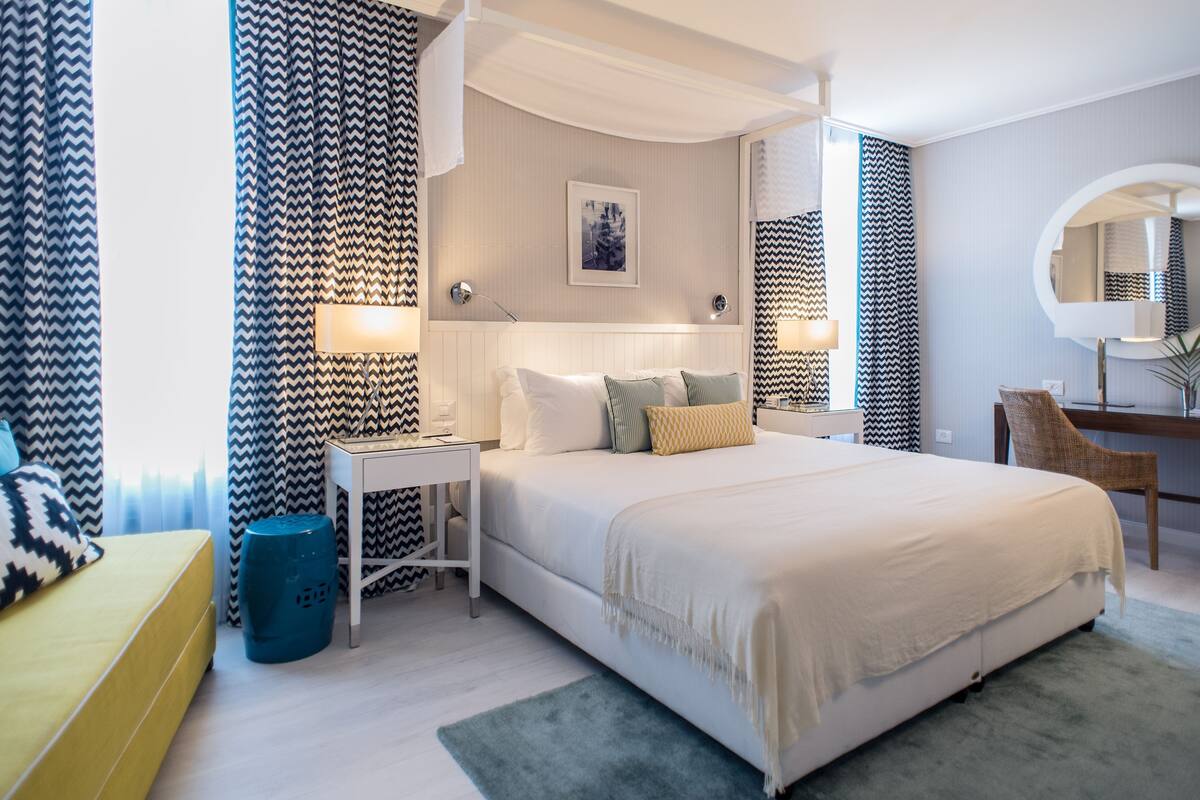 Une chambre à coucher avec un grand lit, des tables de chevet, une chaise et des rideaux à motifs.