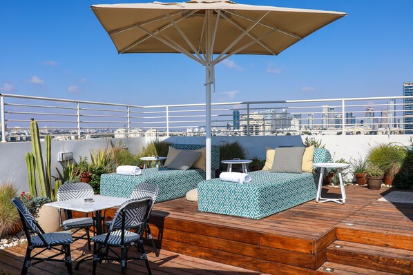 Terraza en la azotea con piso de madera, mobiliario exterior y vistas a la ciudad.