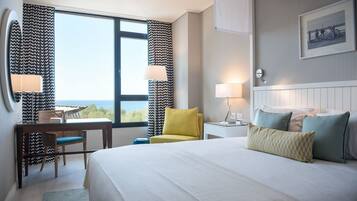 A hotel room with a large bed, a desk with a chair, a small table, and a window with curtains.