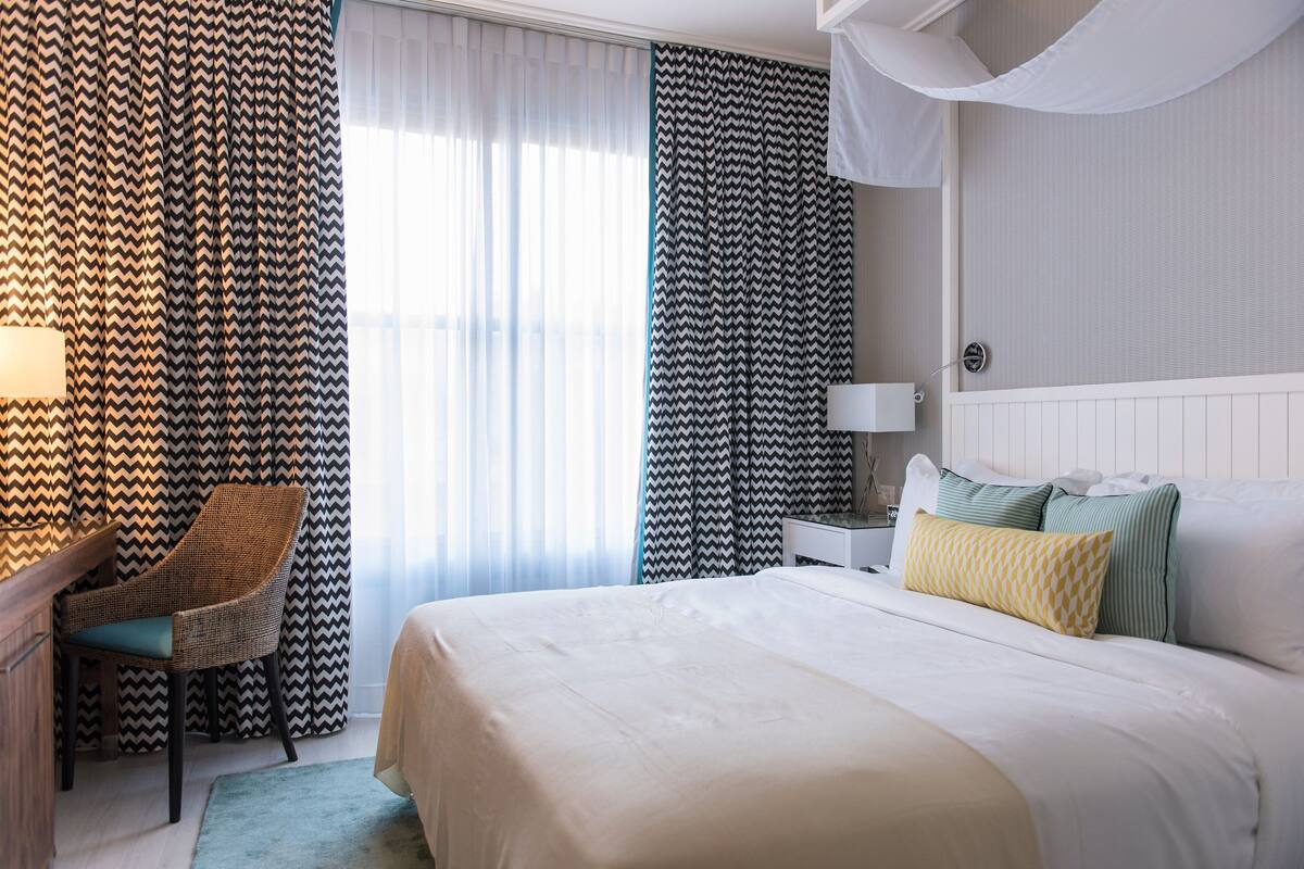 Une chambre d’hôtel avec un grand lit, une chaise, une table de chevet et des rideaux.