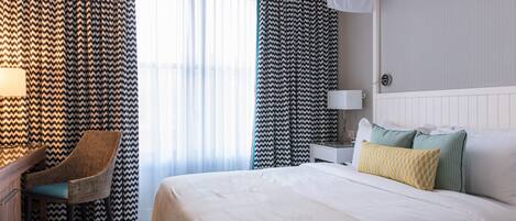 A hotel room with a large bed, a chair, a bedside table, and curtains.