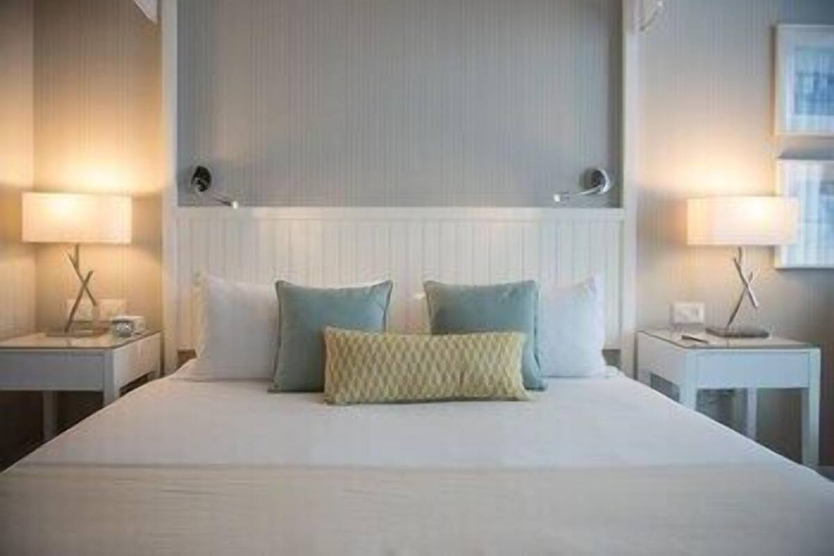 Un lit bien fait, avec des oreillers, une table de chevet avec une lampe et un luminaire fixé au mur.