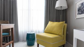 Una habitación con un sillón amarillo, una mesita de madera, una lámpara y un otoman azul.