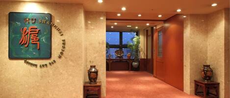 Vestíbulo de hotel con un cartel grande que dice “HU SHANGHAI FUSSI” en la pared, piso alfombrado y un mostrador de recepción con plantas en macetas.