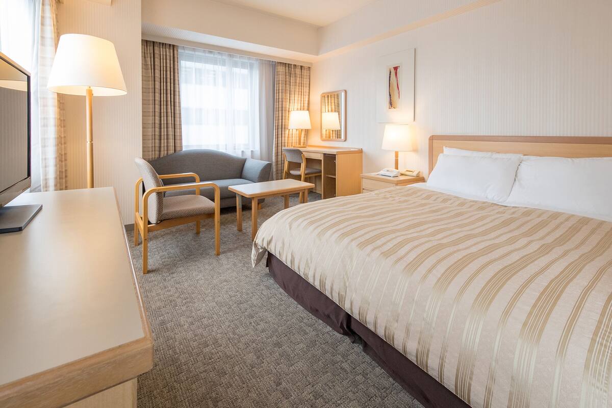 Una habitación de hotel con cama, escritorio, silla, televisor y lámpara.