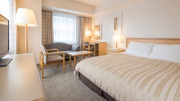 A hotel room with a bed, a desk, a chair, a TV, and a lamp.