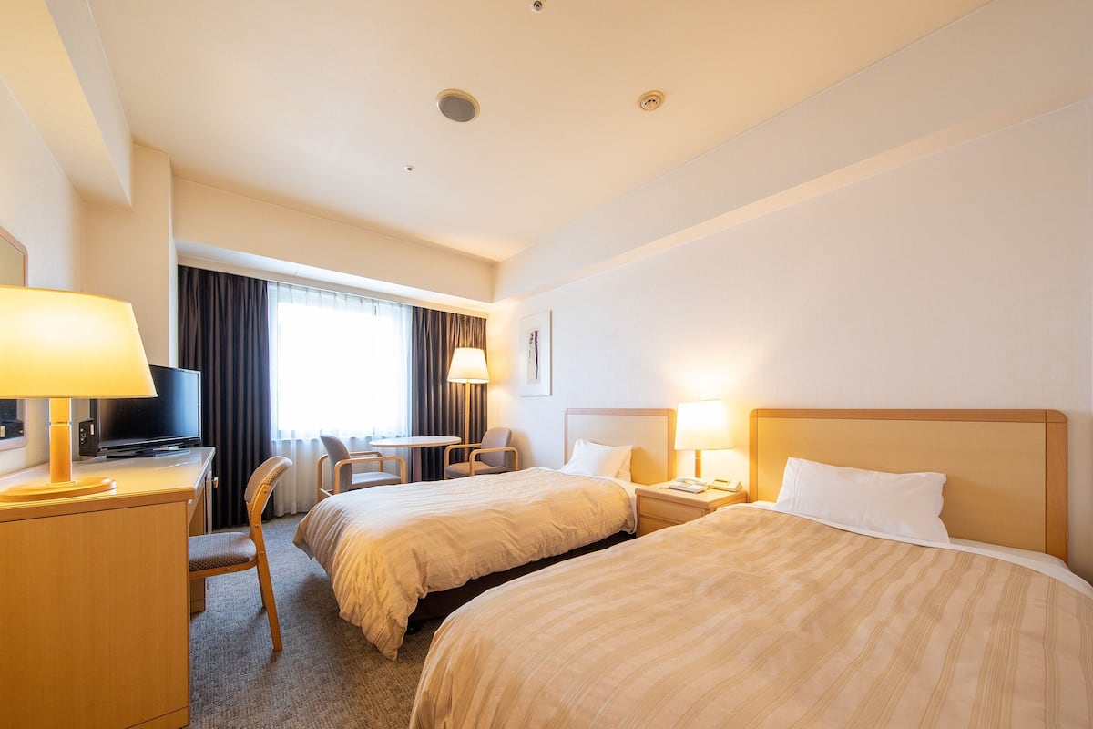 Una habitación de hotel con dos camas, un escritorio, un televisor, una silla y una lámpara.