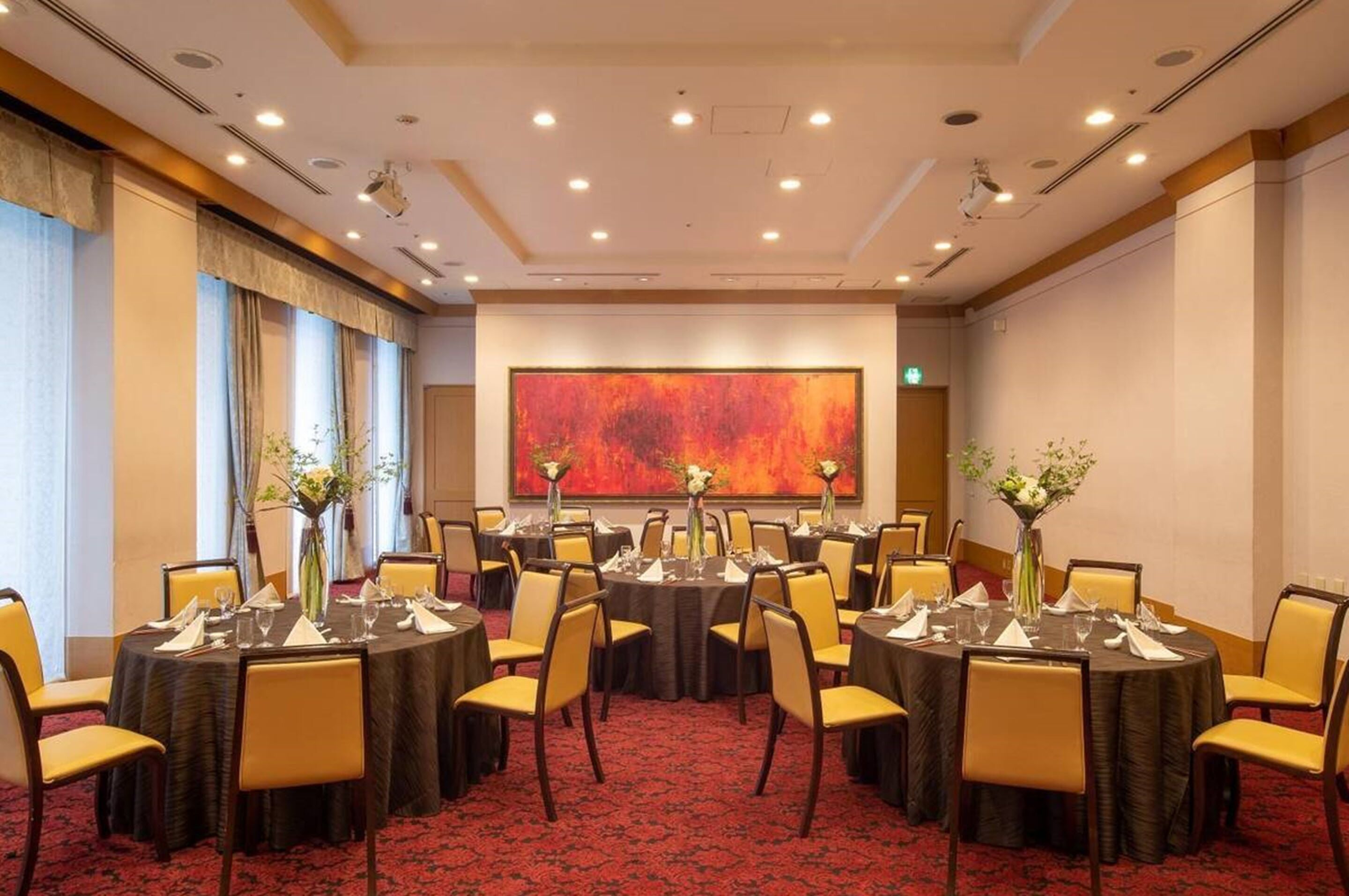 A conference room with round tables, yellow chairs, and a large abstract painting on the wall.