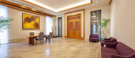 A spacious lobby with a marble floor, a reception desk, a large painting, and a purple sofa.