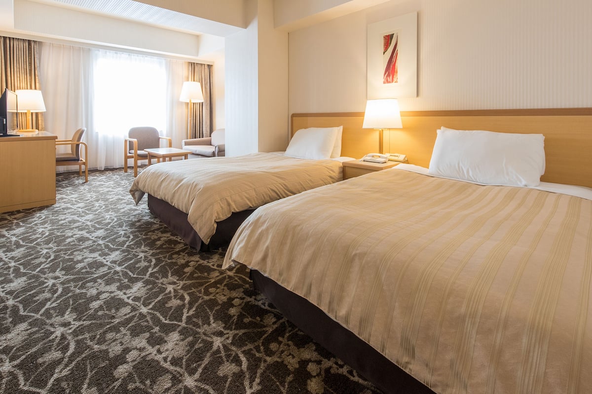 Una habitación de hotel con dos camas, un escritorio, una silla y una lámpara.