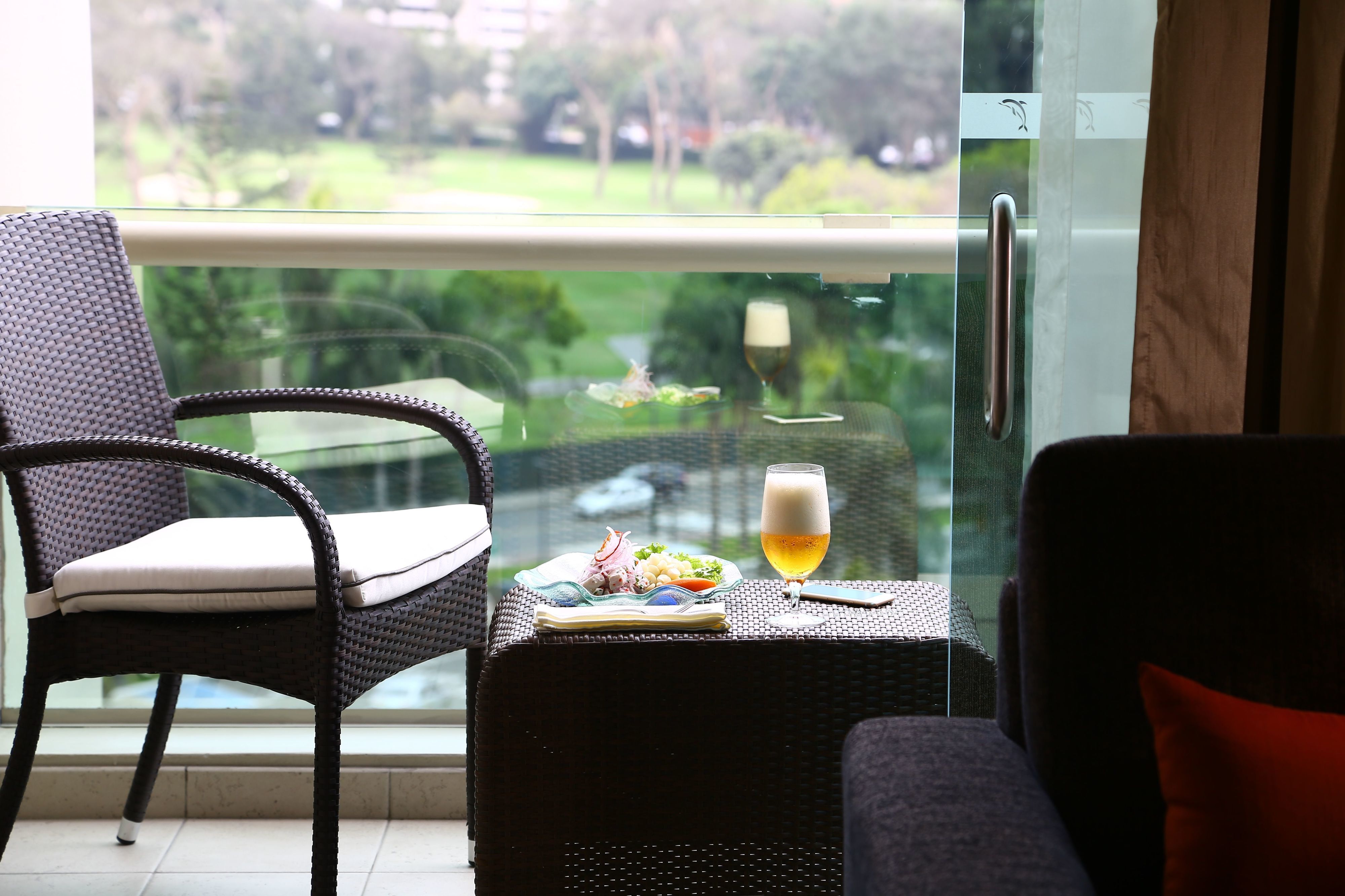 Un balcón con sillones de mimbre, una mesa con una cerveza en un vaso y un plato de comida.