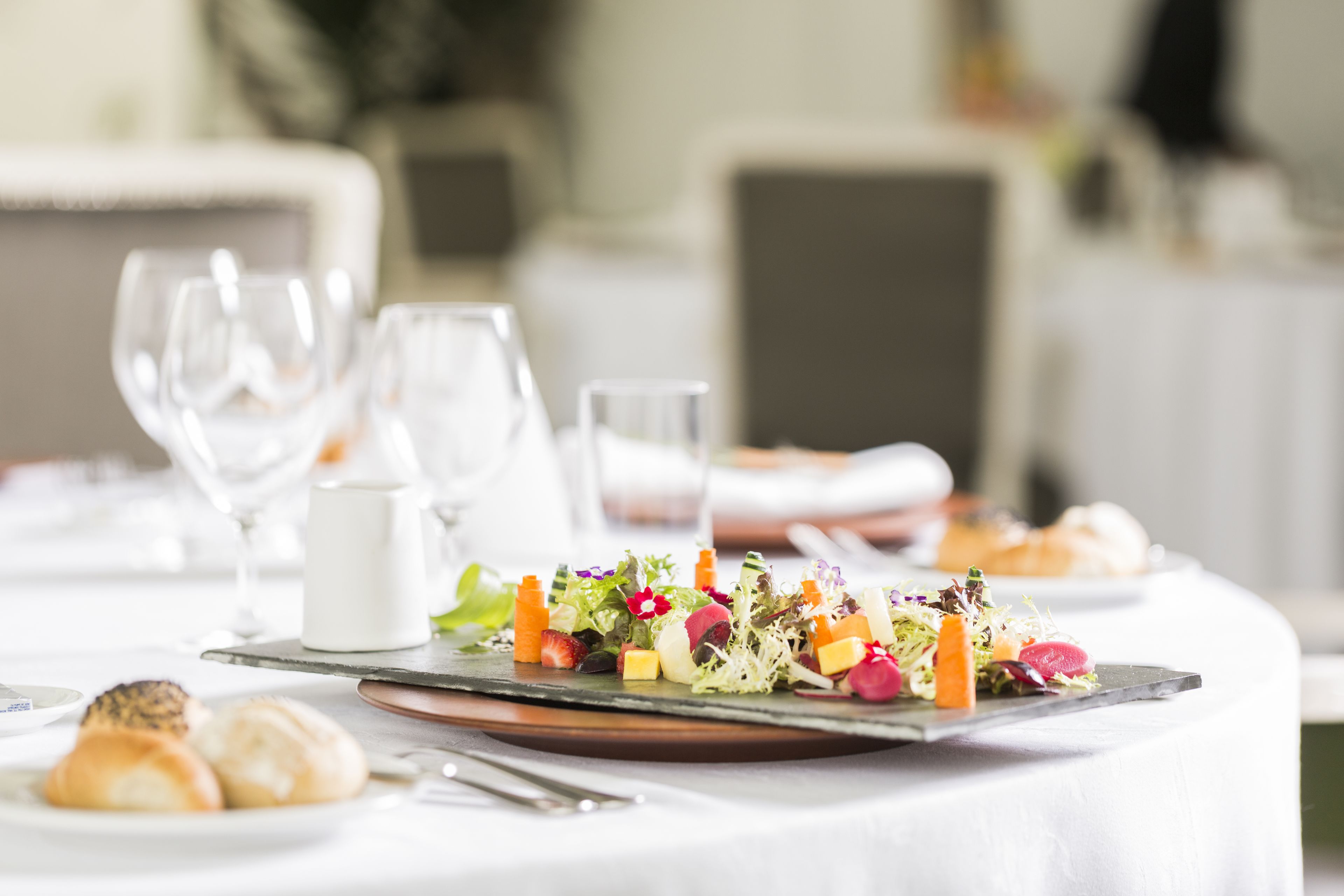 Una mesa de comedor dispuesta con una variedad de platos, incluyendo una ensalada, pan y un plato pequeño con pasteles.