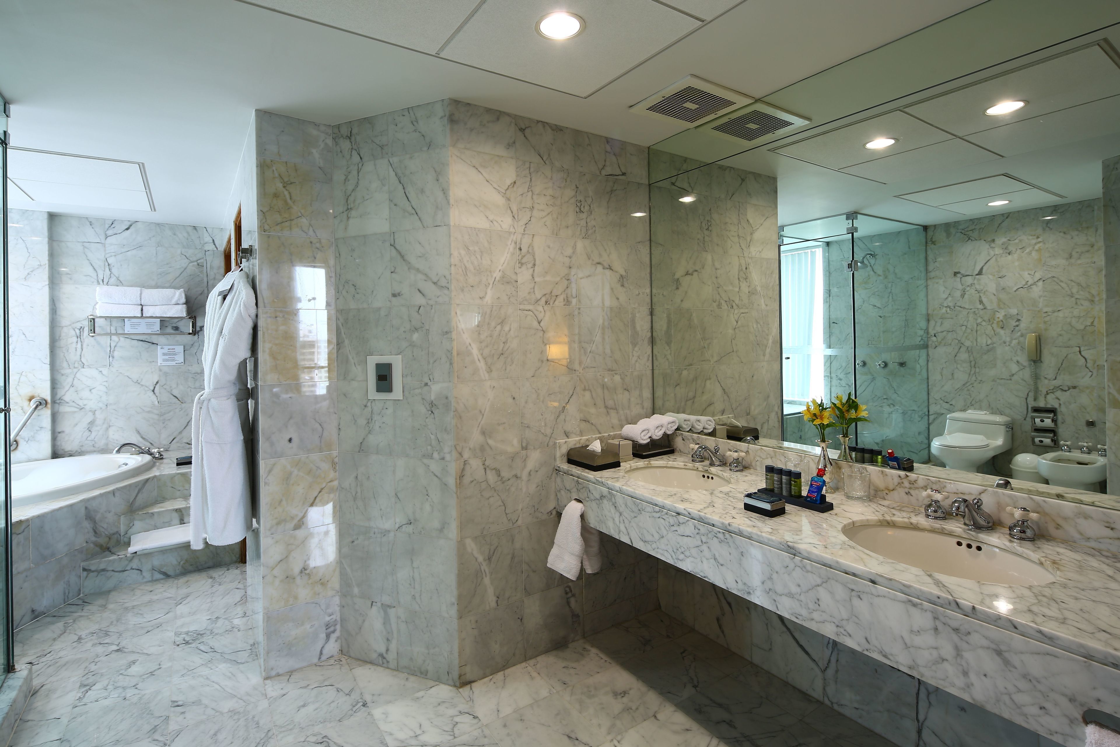 A modern bathroom with marble walls, a large mirror, a bathtub, and a vanity with a sink and toiletries.
