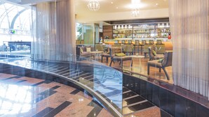 Un moderno vestíbulo de hotel con barandilla de vidrio, zona de estar y barra con una exhibición de licores.