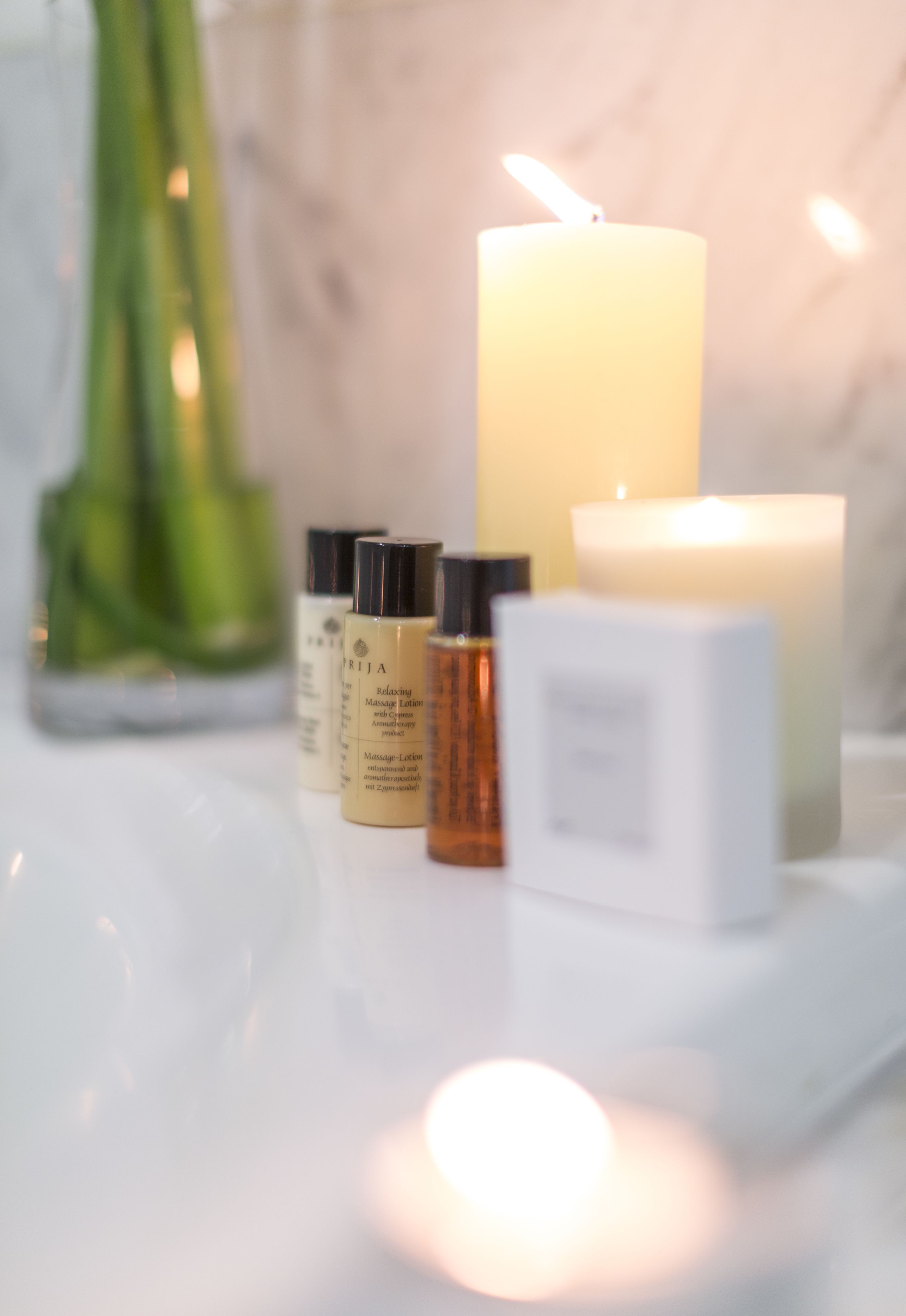A candle, a green vase, and three bottles of lotion on a white surface.