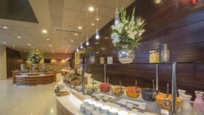 Zona de bufé con diferentes opciones de comida y una barra con platos y recipientes.