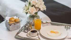 Una bandeja de desayuno ordenada sobre una cama de hotel, con un ramo de flores, un vaso de jugo de naranja y un plato con dos huevos fritos.