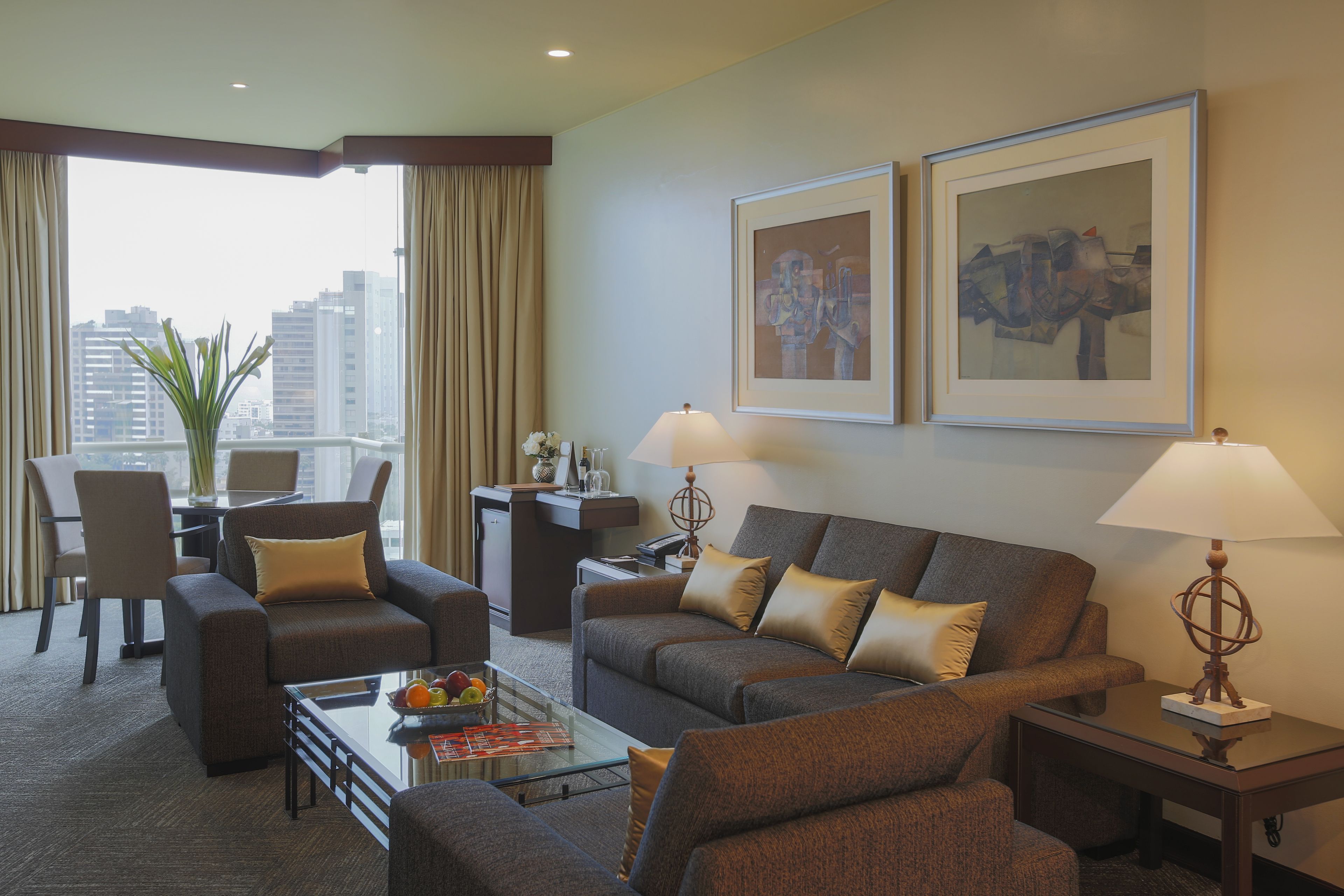 Una habitación de hotel moderna con un conjunto de sofás, un comedor y un amplio ventanal con vistas a la ciudad.