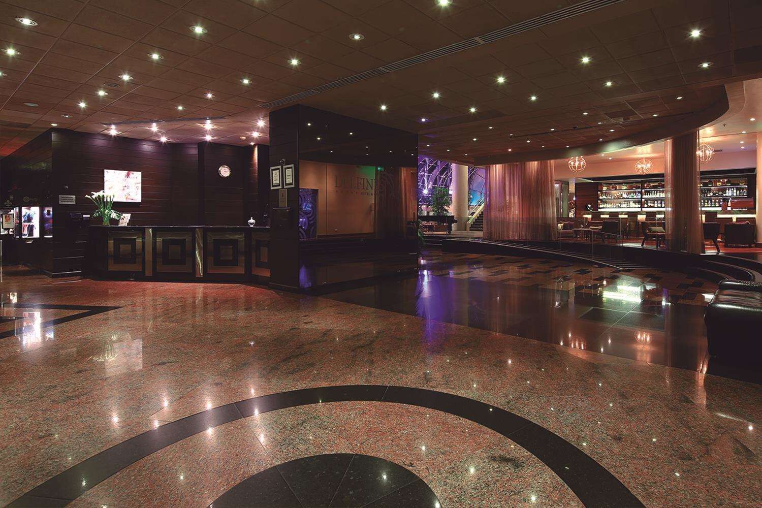 A lobby with a polished marble floor, a reception desk, and a bar area with a visible staircase.
