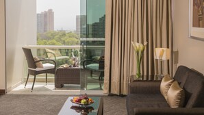 Una habitación de hotel con balcón, zona de comedor con mesa y sillas, sofá y un jarrón con flores.