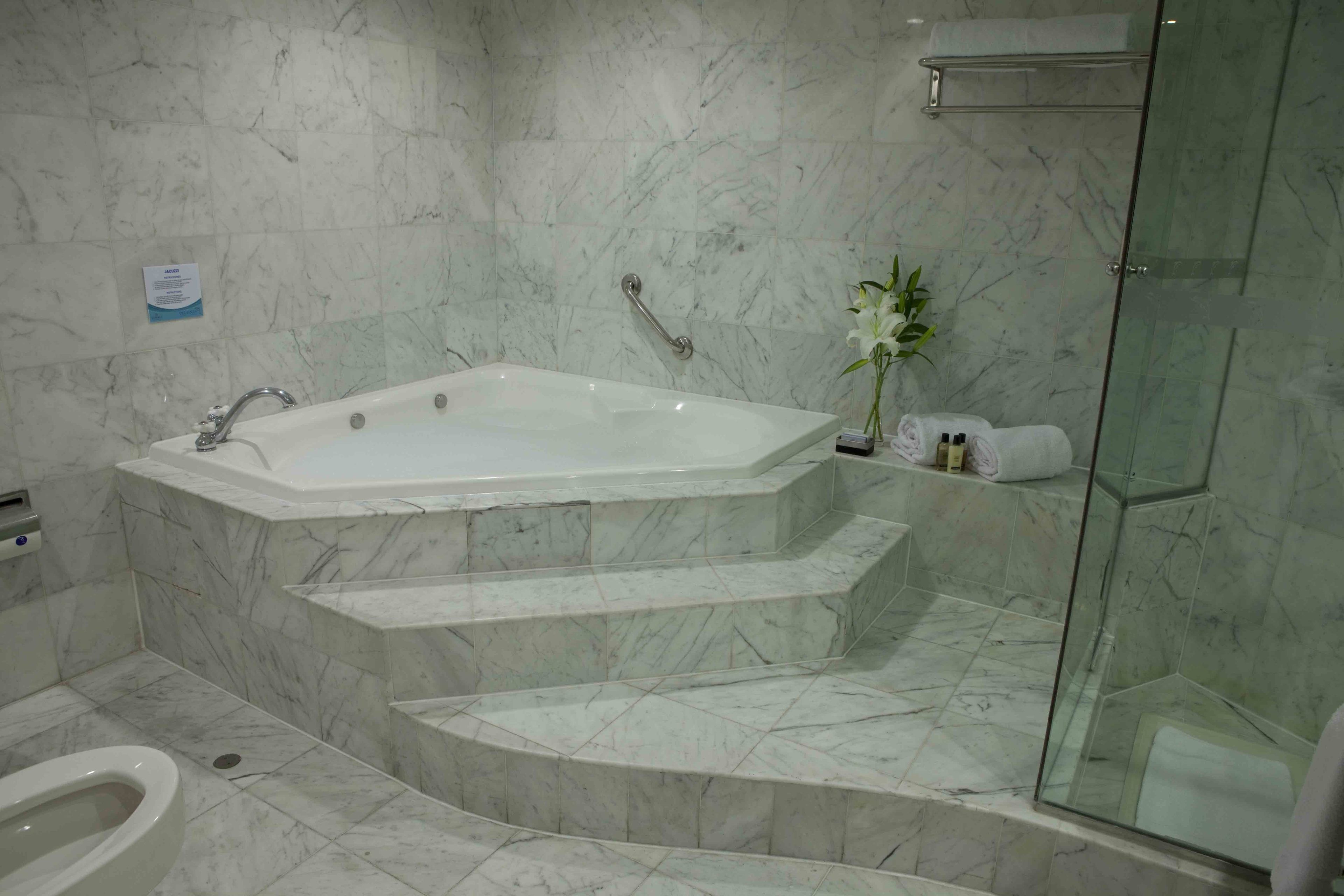 A bathroom with a marble floor, a freestanding bathtub, a glass shower enclosure, and a toilet.