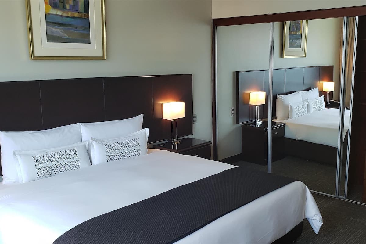 Quarto de hotel com uma cama grande, luminárias de cabeceira, um espelho, um guarda-roupa e uma máquina de café.