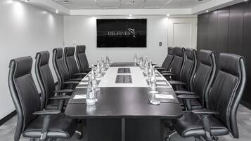 Un salón de conferencias con una larga mesa, sillas de cuero negro y una pantalla grande que muestra 'DELFINES HOTEL & CONVENTION CENTER'.