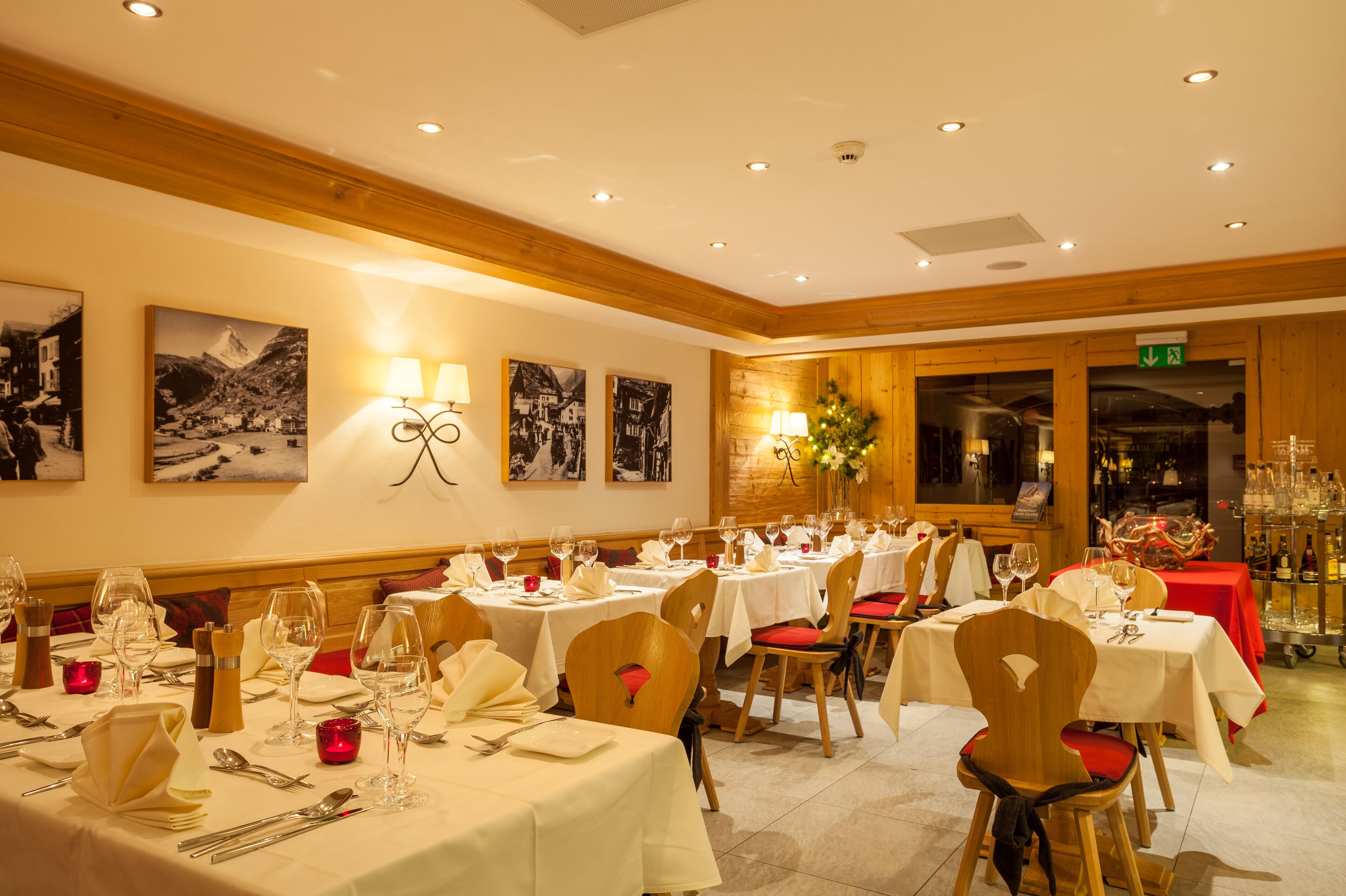 A dining area with multiple tables set for guests, featuring white tablecloths and red cushioned chairs.